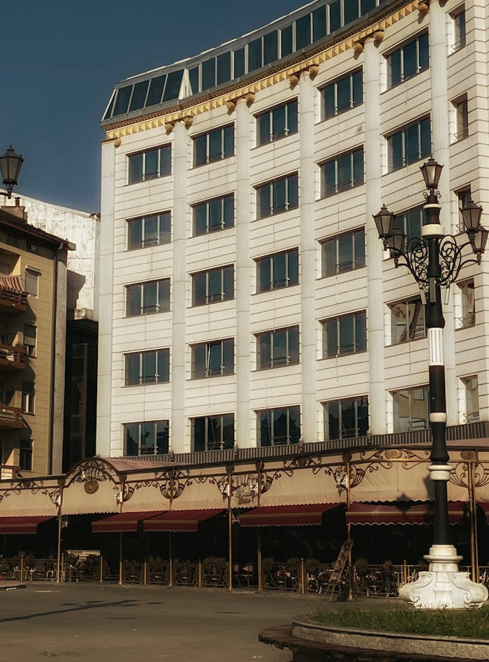 Elegant hotel building with outdoor cafe seating in Üsküp, North Macedonia, under a clear sky.